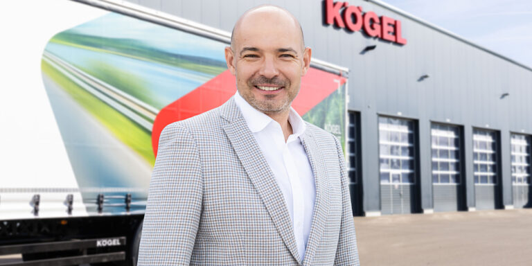 Andrzej Mowczan, dyrektor zarządzający Kögel Polska, na tle naczepy i hali z logo Kögel
